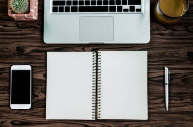 Kahverengi ahşap masa üzerinde bir kitap, kalem, kaktüs ve telefon var..