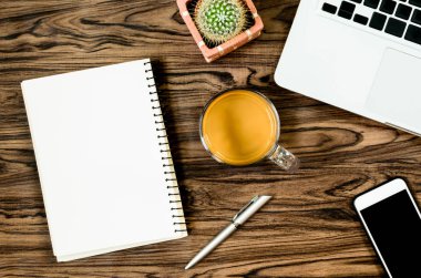 Kahverengi ahşap masa üzerinde bir kitap, kalem, kaktüs ve telefon var..