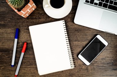 Kahverengi ahşap masa üzerinde bir kitap, kalem, kaktüs ve telefon var..