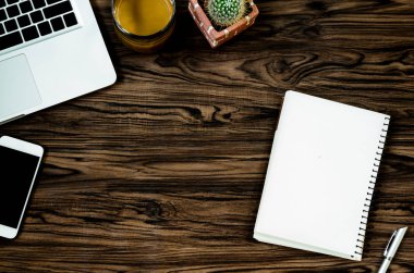 Kahverengi ahşap masa üzerinde bir kitap, kalem, kaktüs ve telefon var..