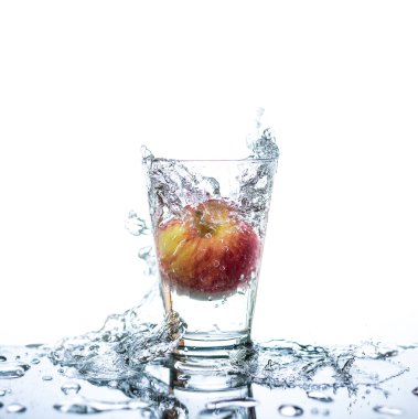 Red apple has droping to the glass and splashing water around the glass and on the table with reflection and isolated white background. clipart