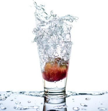 Kırmızı elma cam ve cam etrafında su sıçraması ve yansıma ve izole beyaz arka plan ile masaya düşürüyorsun vardır.