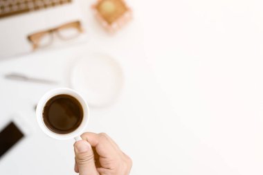İş adamı sabahları çok çalışmak için elinde sade kahve fincanı tutuyor. Masanın üstünde kahve ve bilgisayarla çalışan bir iş adamı..