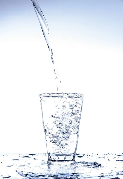 Pouring water and splashing in the glass with reflection on mirror.