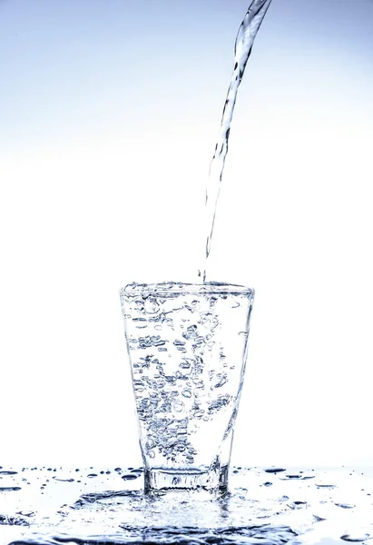 Pouring water and splashing in the glass with reflection on mirror.