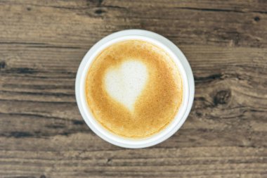 Kahverengi ahşap masa arkasına izole edilmiş, sanat kalbi sütlü bir kahve. Bir fincan kahve ve sevgililer günü konseptiyle yatıyordu..