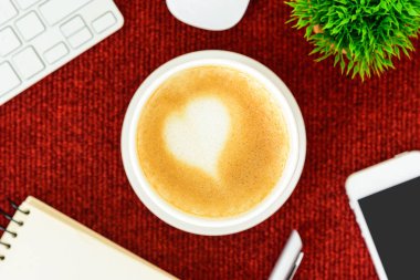 Kırmızı masa masasının üstünde sanat kalbi sütü olan sütlü bir latte kahve. Masa, iş ve sevgililer günü konseptiyle yatıyordu.