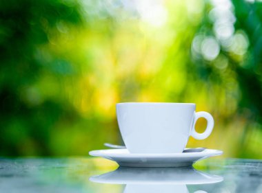 Sabah servis edilecek beyaz bir fincan kahve ve gümüş kaşık. Rahatlatıcı ve sarı ışıklandırma bokeh arka planlı..