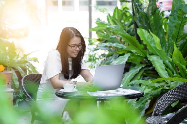 Güzel Asyalı çekici kadın sabahları mutlu ve dinlendirici saatleriyle birlikte iş pazarlaması için dizüstü bilgisayarda çalışıyor ve daktilo kullanıyor..