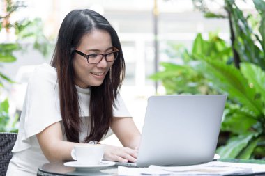 Güzel Asyalı çekici kadın sabahları mutlu ve dinlendirici saatleriyle birlikte iş pazarlaması için dizüstü bilgisayarda çalışıyor ve daktilo kullanıyor..