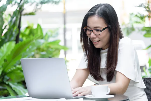 Güzel Asyalı çekici kadın sabahları mutlu ve dinlendirici saatleriyle birlikte iş pazarlaması için dizüstü bilgisayarda çalışıyor ve daktilo kullanıyor..