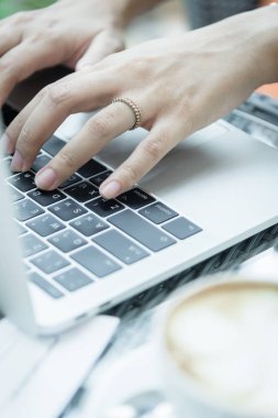 Asyalı kadın elleri ve evlilik yüzüğü laptopta kahve, bilgisayar ve pencerenin dışındaki manzarayla dokunup daktilo ediyor..