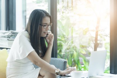 Güzel Asyalı çekici kadın sabahları mutlu ve dinlendirici saatleri olan kahve dükkanında çalışıyor ve iş pazarlaması için telefonla konuşuyor..
