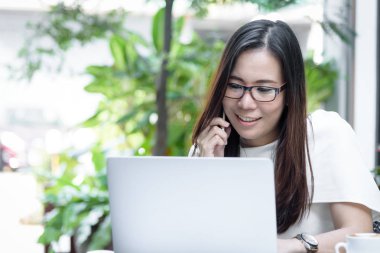 Güzel Asyalı çekici kadın sabahları mutlu ve dinlendirici saatleri olan kahve dükkanında çalışıyor ve iş pazarlaması için telefonla konuşuyor..