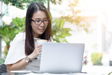 Güzel Asyalı çekici kadın sabahları kahve kafesinde mutlu ve dinlendirici bir şekilde çalışmaya başlamadan önce elinde kahve tutuyor ve içiyor..