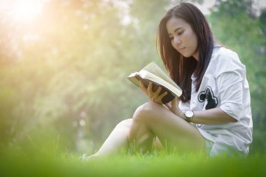 Güzel Asyalı kadın bahçede kitap okuyor. Mutlulukla ve akşamları gün batımında dinleniyor..