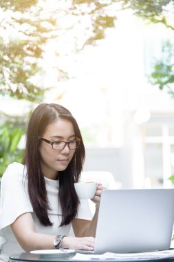 Güzel Asyalı çekici kadın sabahları kahve kafesinde mutlu ve dinlendirici bir şekilde çalışmaya başlamadan önce elinde kahve tutuyor ve içiyor..