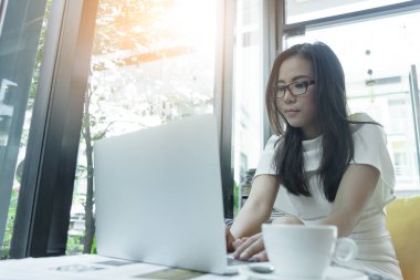Güzel Asyalı çekici kadın sabahları mutlu ve dinlendirici saatleriyle birlikte iş pazarlaması için dizüstü bilgisayarda çalışıyor ve daktilo kullanıyor..