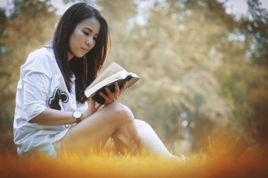 Güzel Asyalı kadın bahçede kitap okuyor. Mutlulukla ve akşamları gün batımında dinleniyor..