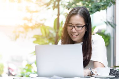 Güzel Asyalı çekici kadın sabahları mutlu ve dinlendirici saatleriyle birlikte iş pazarlaması için dizüstü bilgisayarda çalışıyor ve daktilo kullanıyor..