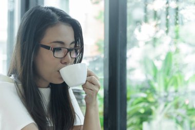 Güzel Asyalı çekici bir kadın sabahları kahve kafesinde mutlu ve dinlendirici bir şekilde kahve içiyor..