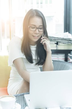 Güzel Asyalı çekici kadın sabahları mutlu ve dinlendirici saatleri olan kahve dükkanında çalışıyor ve iş pazarlaması için telefonla konuşuyor..