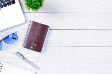 Çalışan ve çalışan masası düz bir manzaradan beyaz ahşap masa üzerinde dizüstü bilgisayar ve pasaportla seyahat etmeye hazırlanıyor ve hayal kuruyor..
