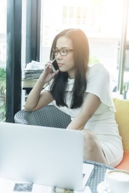 Güzel Asyalı çekici kadın sabahları mutlu ve dinlendirici saatleri olan kahve dükkanında çalışıyor ve iş pazarlaması için telefonla konuşuyor..