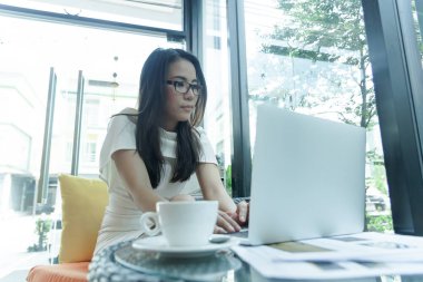 Güzel Asyalı çekici kadın sabahları mutlu ve dinlendirici saatleriyle birlikte iş pazarlaması için dizüstü bilgisayarda çalışıyor ve daktilo kullanıyor..
