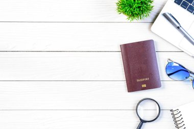 Çalışan ve çalışan masası düz bir manzaradan beyaz ahşap masa üzerinde dizüstü bilgisayar ve pasaportla seyahat etmeye hazırlanıyor ve hayal kuruyor..