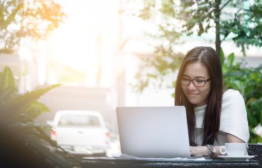 Güzel Asyalı çekici kadın sabahları mutlu ve dinlendirici saatleriyle birlikte iş pazarlaması için dizüstü bilgisayarda çalışıyor ve daktilo kullanıyor..