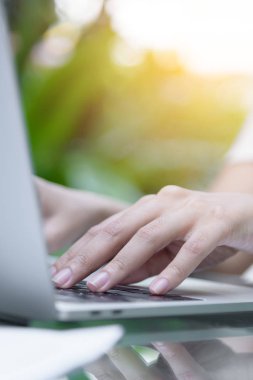 Asyalı kadının elleri bilgisayarında dokunuyor ve daktilo ediyor. Bulanık kahve, bilgisayar ve dışarıyı görüyor..