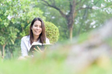 Güzel Asyalı kadın bahçede kitap okuyor. Mutlulukla ve akşamları gün batımında dinleniyor..