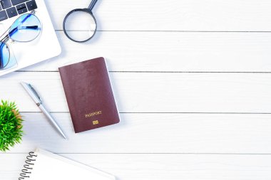 Çalışan ve çalışan masası düz bir manzaradan beyaz ahşap masa üzerinde dizüstü bilgisayar ve pasaportla seyahat etmeye hazırlanıyor ve hayal kuruyor..