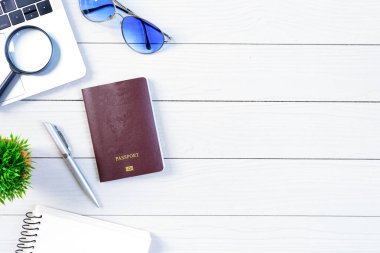 Çalışan ve çalışan masası düz bir manzaradan beyaz ahşap masa üzerinde dizüstü bilgisayar ve pasaportla seyahat etmeye hazırlanıyor ve hayal kuruyor..