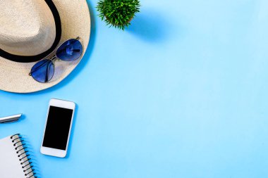 Beyaz şapkalı, mavi gözlüklü, telefon ve not defterli yaz seyahati planlama kavramı mavi arkaplanda izole edilmiş..
