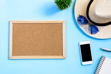 Beyaz şapkalı, mavi gözlüklü, telefon, not defteri ve mavi arka planda izole edilmiş kahverengi tahta tahtalı yaz seyahati konsepti..