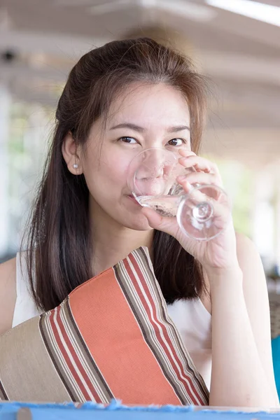 Beautiful asian woman has drinking a glass of water in the bar and restaurant for dinner in the evening and sun lighting with relaxing and vacation time.
