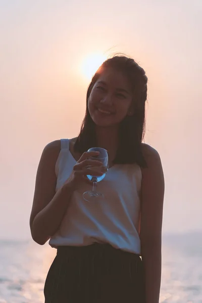 美しいアジアの女性は夕日とスカイラインと夜の時間に海とビーチでワインと酒のグラスを持っています リラックス ファッション ライフスタイル 休暇時間のコンセプト — ストック写真