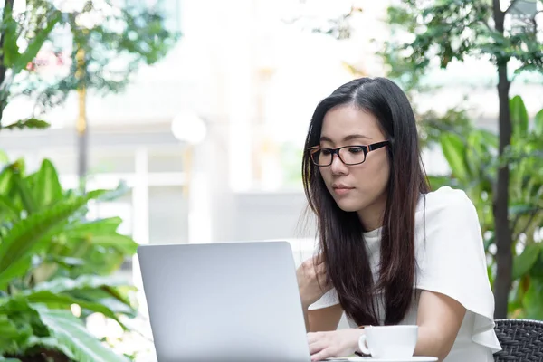 Güzel Asyalı çekici kadın sabahları mutlu ve dinlendirici saatleriyle birlikte iş pazarlaması için dizüstü bilgisayarda çalışıyor ve daktilo kullanıyor..