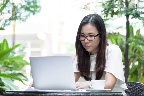 Güzel Asyalı çekici kadın sabahları mutlu ve dinlendirici saatleriyle birlikte iş pazarlaması için dizüstü bilgisayarda çalışıyor ve daktilo kullanıyor..