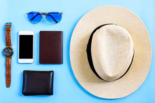 Top view summer travel planning concept with white hat, blue eyeglasses, phone, watch, blank passport and brown wallet isolated on blue background.