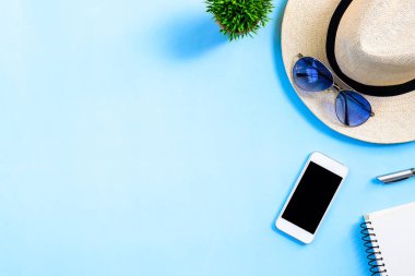 Beyaz şapkalı, mavi gözlüklü, telefon ve not defterli yaz seyahati planlama kavramı mavi arkaplanda izole edilmiş..