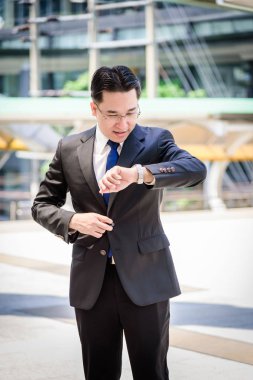 Asyalı işadamının elinde siyah bir çanta var ve aceleyle nöbet tutuyor..