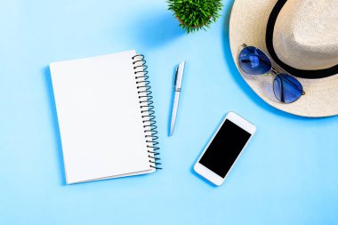 Beyaz şapkalı, mavi gözlüklü, telefon ve not defterli yaz seyahati konsepti mavi arka planda izole edilmiş..