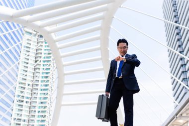 Asyalı işadamının elinde siyah bir çanta var ve aceleyle nöbet tutuyor..