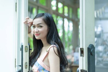 Asyalı güzel kız, Tayland 'ın Nakhon Pathom bölgesindeki Küçük Ağaç Bahçesi Kafesi' nde mutlu ve gülümseyerek kapıyı açıyor..