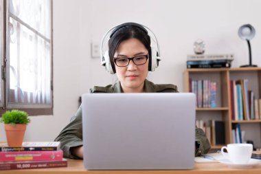 Modern genç Asyalı kadın evden çalışıyor ve beyaz kulaklıklı müzik dinliyor..