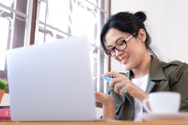 Modern genç Asyalı kadın evden çalışmaya başlamadan önce jel temizleyicisiyle el temizliği yapıyor..