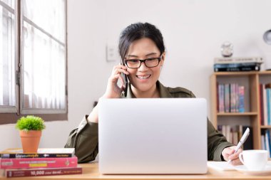 Modern, genç Asyalı bir kadın evde çalışıyor ve mutlu bir şekilde iş ortağı ile konuşuyor..